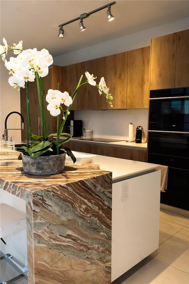 kitchen with track lighting, light tile patterned floors, cooktop, double oven, and sink