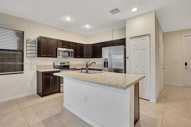 kitchen with light tile patterned floors, a center island with sink, stainless steel appliances, dark brown cabinets, and sink