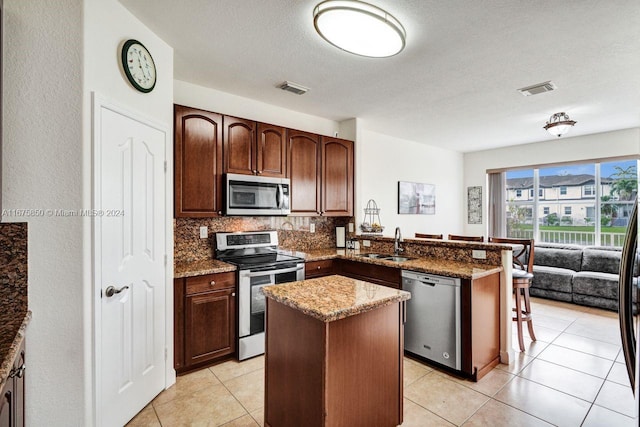 kitchen with a textured ceiling, a center island, kitchen peninsula, stainless steel appliances, and dark stone countertops