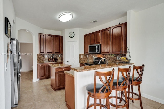 kitchen with kitchen peninsula, light stone counters, backsplash, a breakfast bar area, and stainless steel appliances