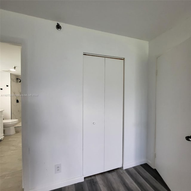 unfurnished bedroom featuring a closet, ensuite bath, and dark wood-type flooring