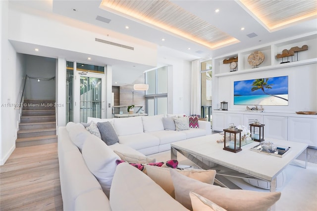 living room with a tray ceiling and light wood-type flooring