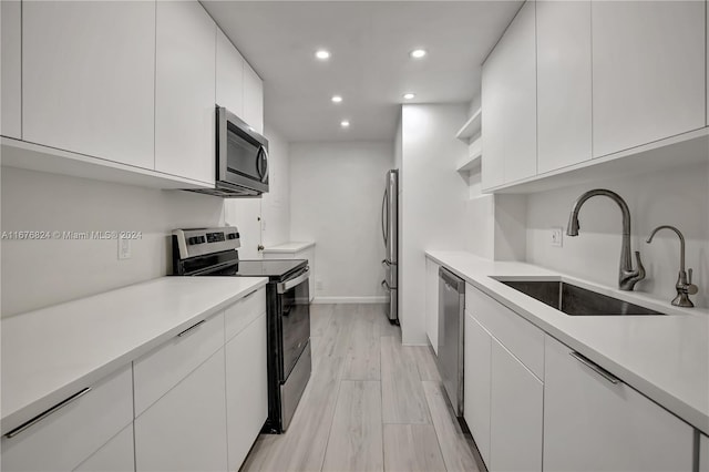 kitchen featuring appliances with stainless steel finishes, sink, light wood-type flooring, and white cabinets