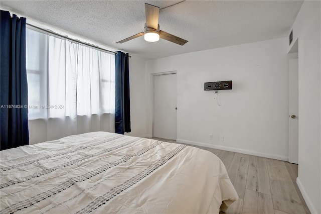 bedroom with light hardwood / wood-style flooring, a textured ceiling, and ceiling fan