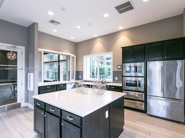 kitchen featuring a kitchen island, appliances with stainless steel finishes, light stone counters, light hardwood / wood-style floors, and tasteful backsplash