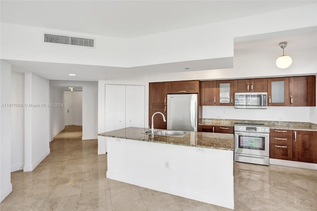 kitchen featuring stone counters, sink, hanging light fixtures, stainless steel appliances, and a center island with sink