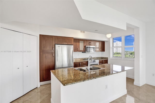 kitchen with sink, an island with sink, stainless steel appliances, dark stone countertops, and light tile patterned floors