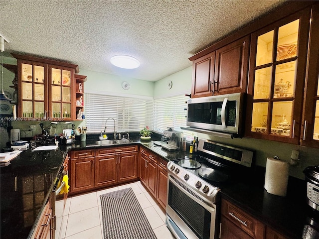 kitchen featuring sink, dark stone countertops, a textured ceiling, light tile patterned floors, and appliances with stainless steel finishes