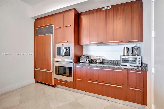 kitchen featuring light tile patterned floors, double oven, paneled built in fridge, and dark stone countertops