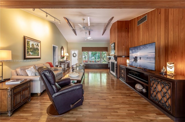 living room featuring vaulted ceiling with beams, wood walls, light wood-type flooring, and ceiling fan