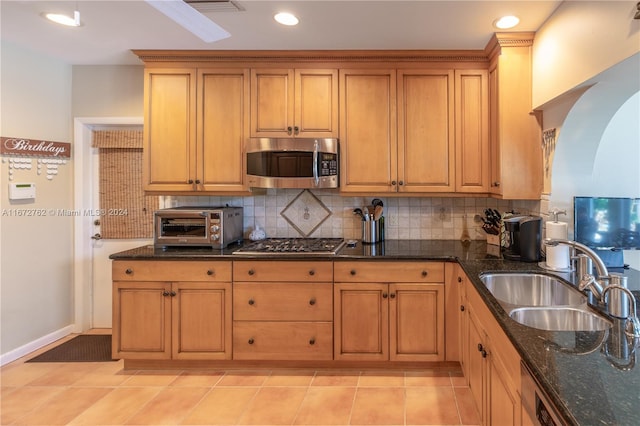 kitchen featuring appliances with stainless steel finishes, sink, backsplash, dark stone counters, and light tile patterned floors