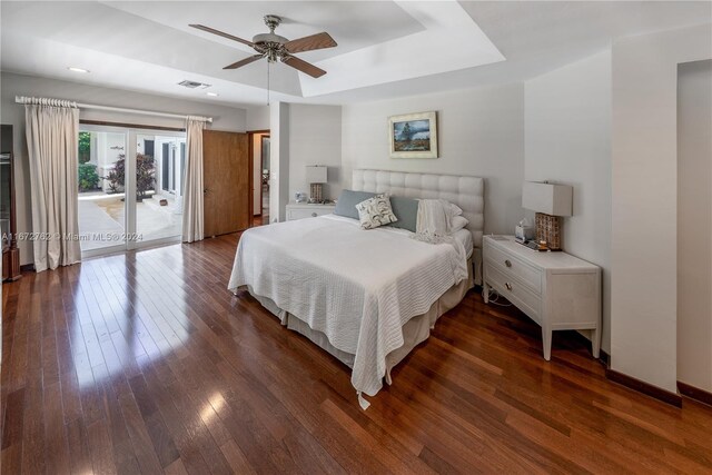 bedroom with dark wood-type flooring, ceiling fan, a raised ceiling, and access to exterior