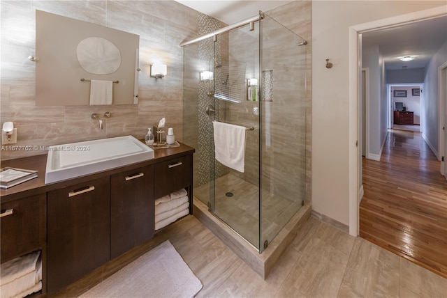 bathroom with a shower with door, vanity, hardwood / wood-style floors, and tile walls