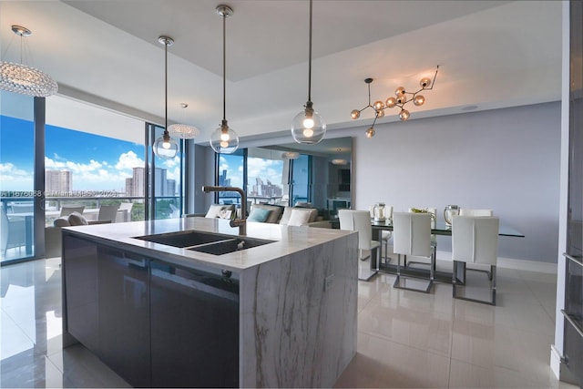 kitchen featuring a kitchen island with sink, hanging light fixtures, sink, light tile patterned flooring, and expansive windows