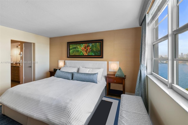 bedroom featuring ensuite bath, a water view, and dark colored carpet