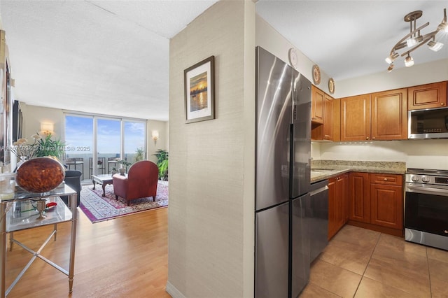 kitchen featuring a wall of windows, light wood-type flooring, light stone counters, and stainless steel appliances