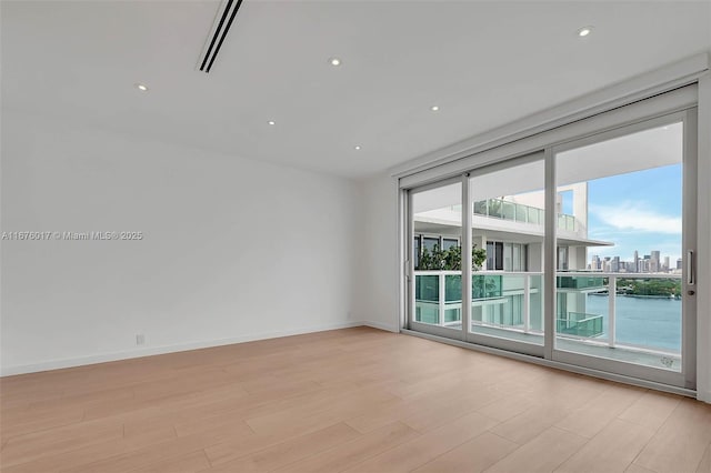 unfurnished room featuring a water view, light wood-type flooring, and a wall of windows