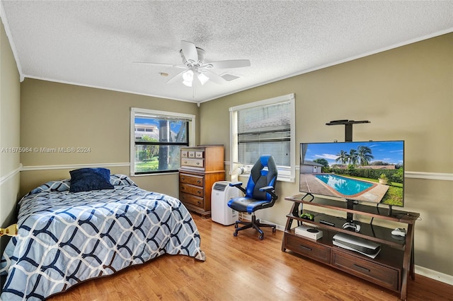 bedroom with ornamental molding, light hardwood / wood-style floors, a textured ceiling, and ceiling fan