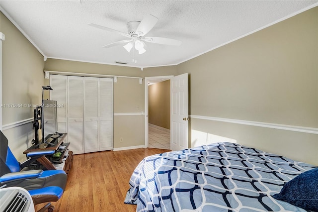 bedroom featuring a closet, ornamental molding, a textured ceiling, ceiling fan, and light hardwood / wood-style flooring