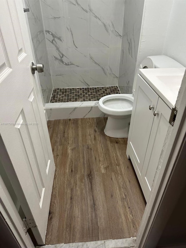 bathroom with toilet, vanity, tiled shower, and hardwood / wood-style floors