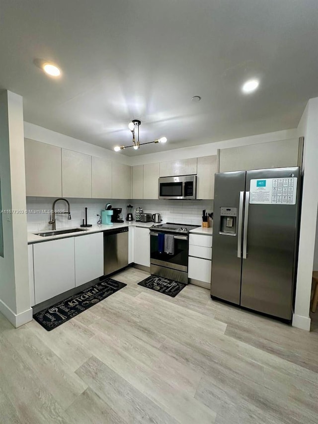 kitchen featuring stainless steel appliances, an inviting chandelier, decorative backsplash, sink, and light wood-type flooring