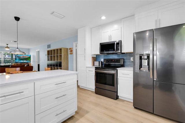 kitchen with tasteful backsplash, white cabinetry, stainless steel appliances, pendant lighting, and light hardwood / wood-style flooring