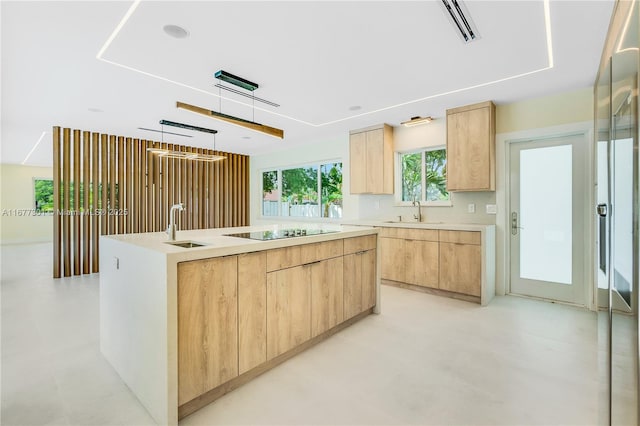 kitchen with black electric cooktop, sink, an island with sink, and light brown cabinets