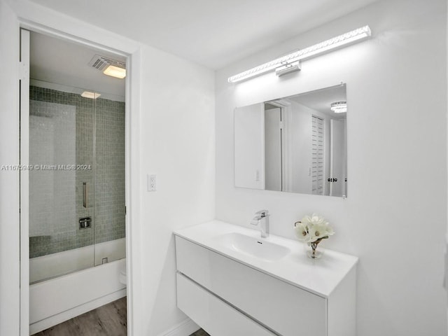 full bathroom featuring vanity, toilet, hardwood / wood-style flooring, and bath / shower combo with glass door