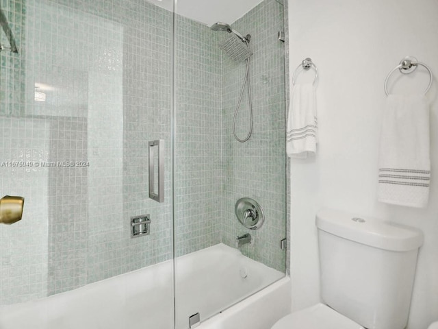 bathroom featuring toilet and shower / bath combination with glass door