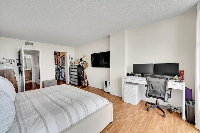 bedroom with a closet, a textured ceiling, a walk in closet, and light wood-type flooring