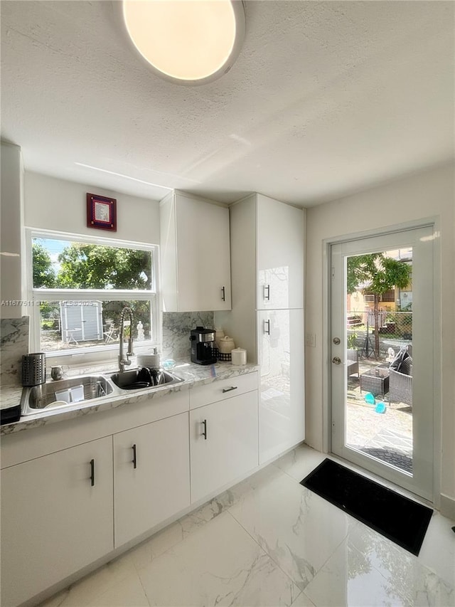 kitchen featuring sink, a wealth of natural light, white cabinets, and backsplash