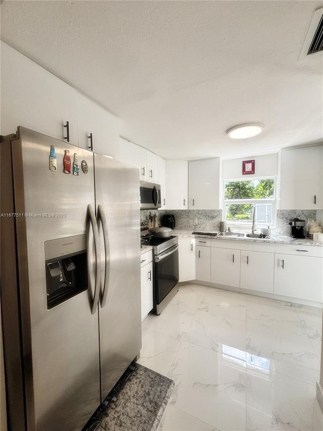 kitchen with sink, stainless steel appliances, white cabinets, a textured ceiling, and decorative backsplash