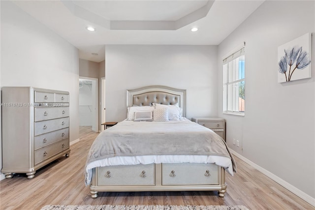 bedroom with a spacious closet, a closet, a tray ceiling, and light hardwood / wood-style floors