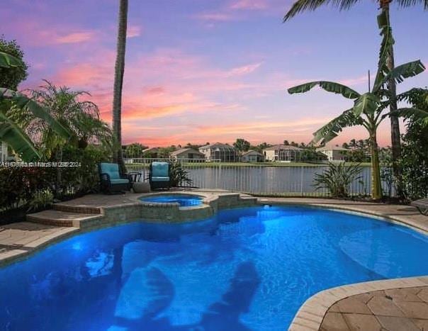 pool at dusk with an in ground hot tub and a water view