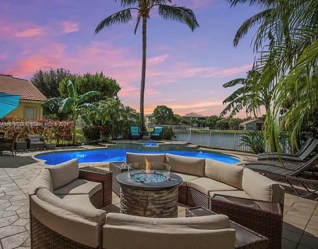 pool at dusk with a patio and an outdoor living space with a fire pit