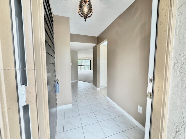 hallway with a textured ceiling and light tile patterned flooring