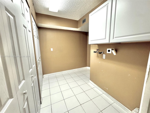 washroom with cabinets, a textured ceiling, light tile patterned flooring, and electric dryer hookup