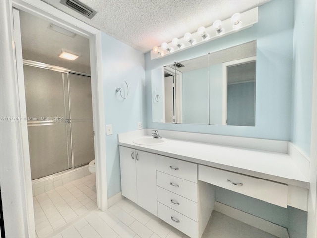 bathroom featuring a shower with door, tile patterned floors, toilet, vanity, and a textured ceiling