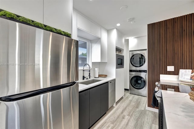 kitchen featuring appliances with stainless steel finishes, sink, white cabinetry, stacked washer / drying machine, and light hardwood / wood-style flooring