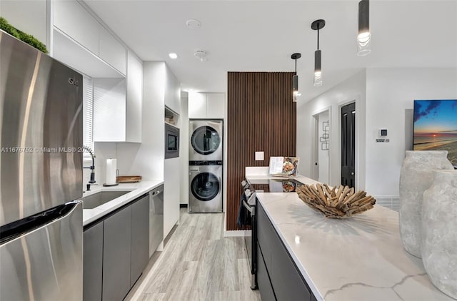 kitchen with stacked washer and dryer, sink, pendant lighting, appliances with stainless steel finishes, and light hardwood / wood-style floors