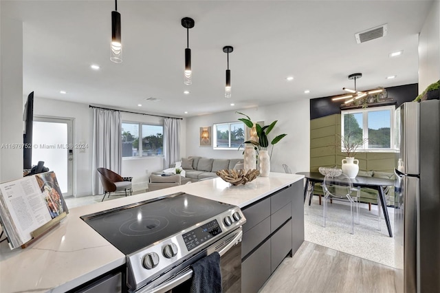 kitchen with light hardwood / wood-style floors, stainless steel appliances, pendant lighting, and light stone counters