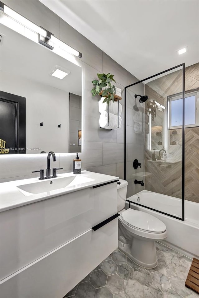 full bathroom featuring vanity, toilet, tile walls, and bath / shower combo with glass door