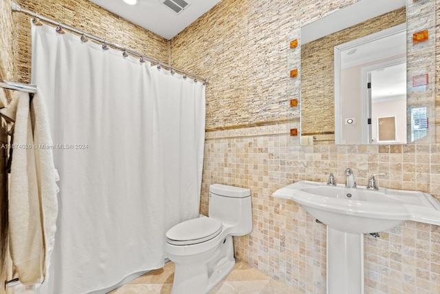 bathroom featuring toilet, sink, tile walls, and tile patterned flooring