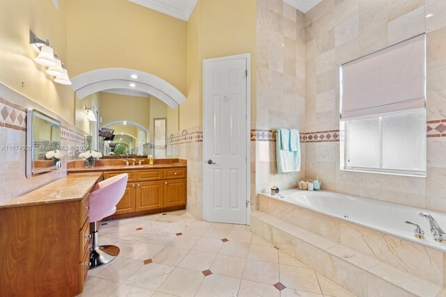 bathroom with a relaxing tiled tub, tile walls, a high ceiling, vanity, and ornamental molding