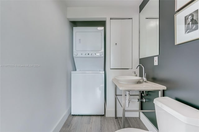 bathroom with toilet, hardwood / wood-style floors, stacked washer and dryer, and sink