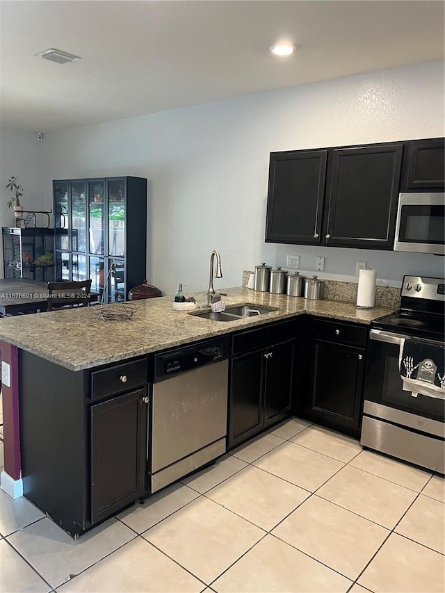 kitchen with sink, kitchen peninsula, stainless steel appliances, light stone counters, and light tile patterned floors