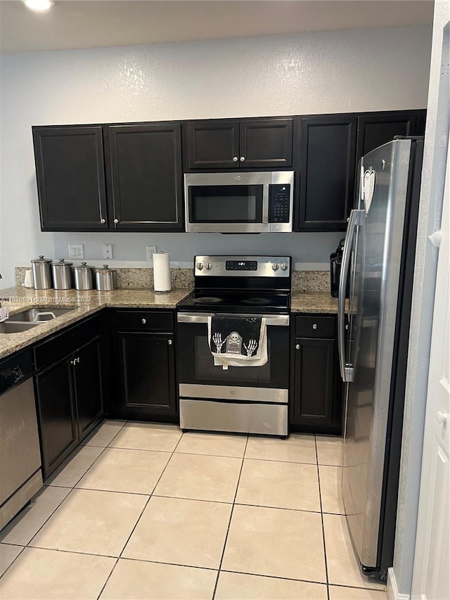 kitchen with sink, appliances with stainless steel finishes, light stone counters, and light tile patterned floors