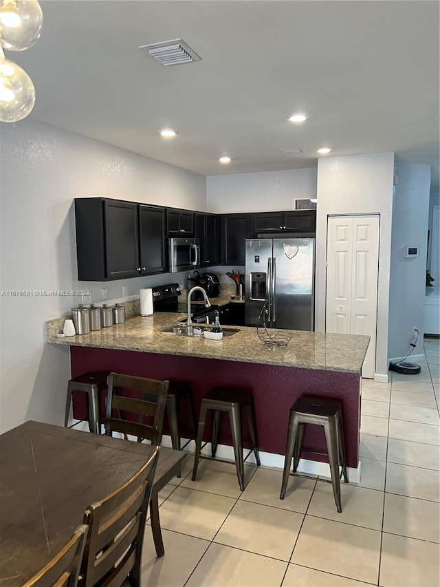 kitchen featuring kitchen peninsula, light tile patterned floors, a breakfast bar, sink, and stainless steel appliances