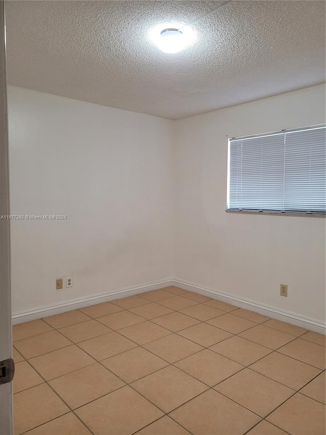 spare room with a textured ceiling and light tile patterned flooring