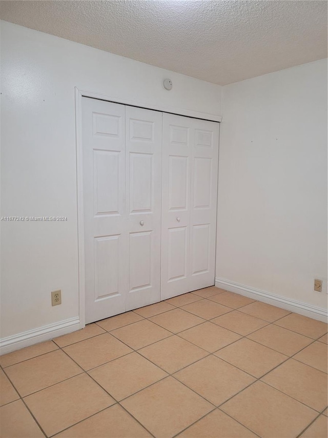 unfurnished bedroom featuring a textured ceiling, a closet, and light tile patterned floors